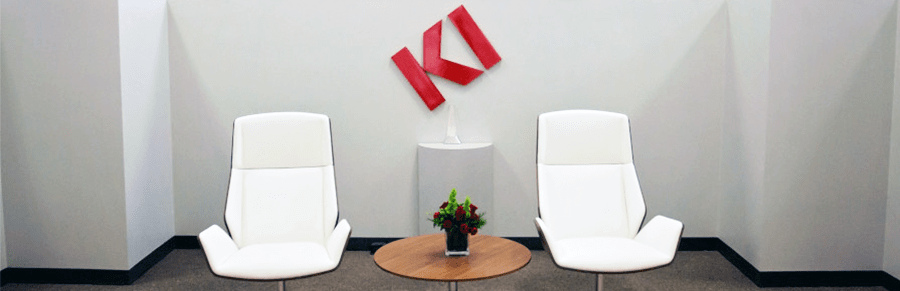 Two white modern chairs in a lobby with the KI logo on the wall behind them